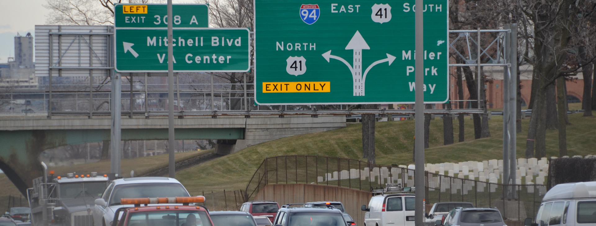 Traffic backed up on the I-94 East-West corridor in Milwaukee beneath overhead signs for Exit 308A, Mitchell Boulevard, the VA Center, and Miller Park Way