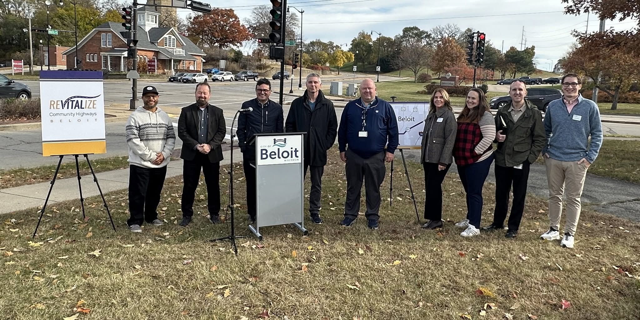 Local officials and community leaders gathered at a Revitalize Community Highways event in Beloit, beside a City of Beloit podium and project signage